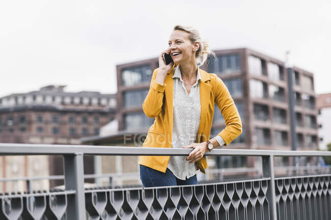 Счастливая деловая женщина разговаривает через мобильный телефон, опираясь на перила — стоковое фото