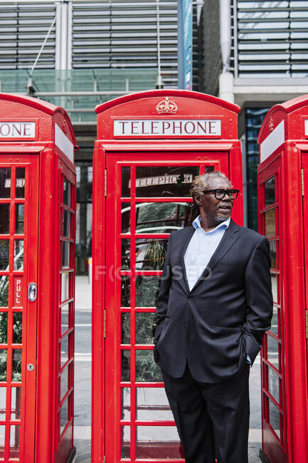 Businessman with hands in pockets standing near telephone booth — Stock Photo