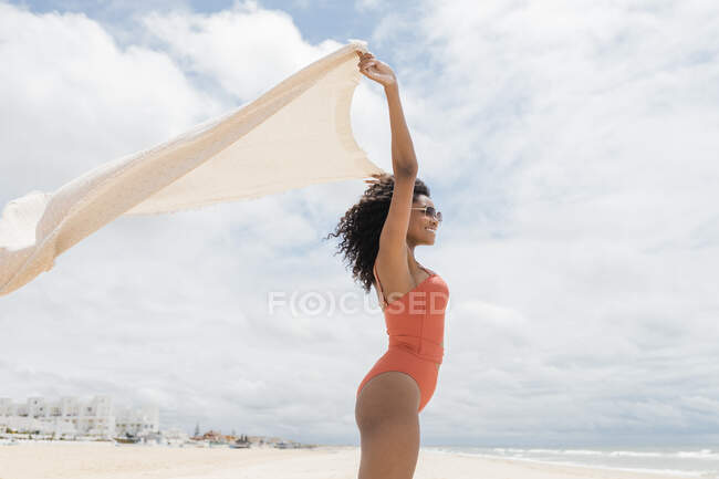 Donna sorridente che tiene l'asciugamano mentre si trova in spiaggia — Foto stock