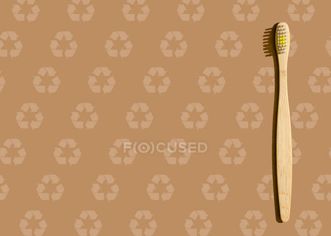 Studio colpo di spazzolino da denti in legno sdraiato contro modello marrone con simboli di riciclaggio — Foto stock
