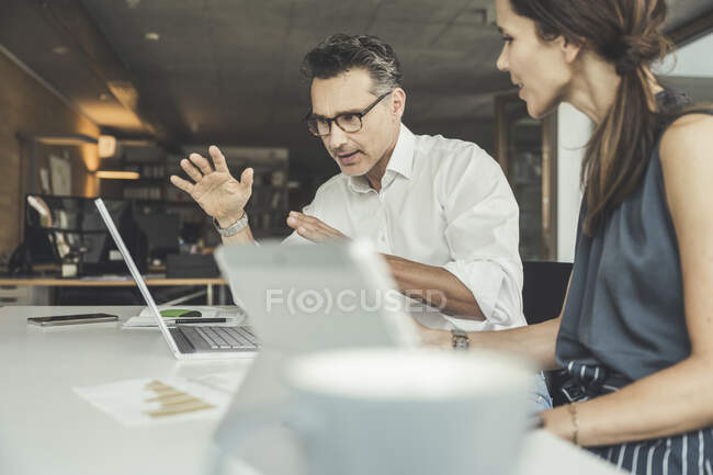 Homme professionnel expliquant sur ordinateur portable à une collègue féminine au bureau — Photo de stock