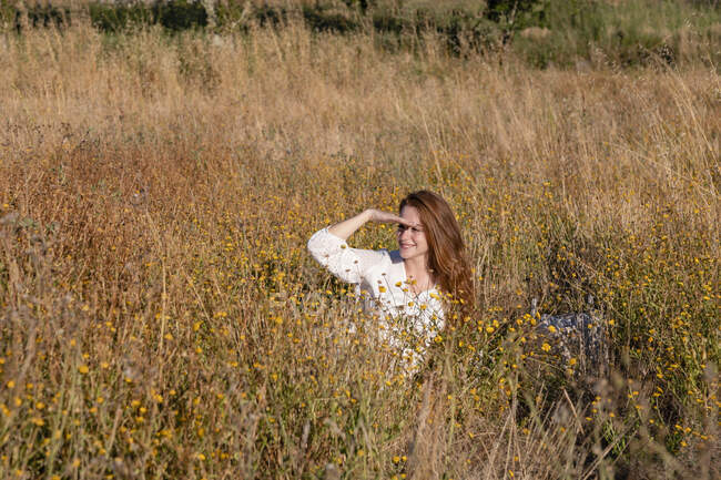 Sorridente giovane donna schermatura gli occhi mentre distoglie lo sguardo sul campo — Foto stock