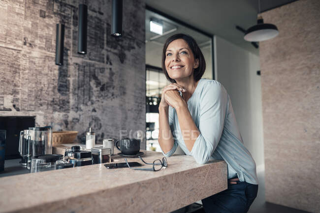 Жіночий підприємець відводить погляд убік, спираючись на стіл у офісі. — стокове фото