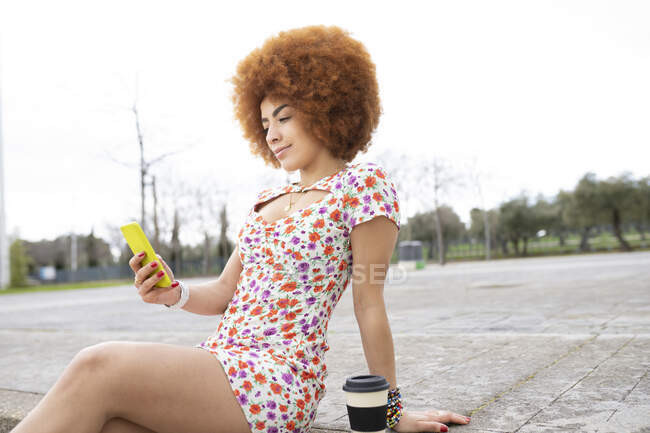 Woman in floral dress using mobile phone while sitting on footpath — Stock Photo