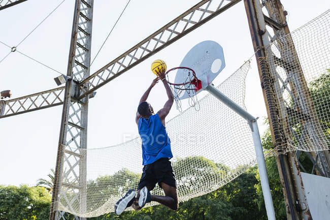 Jeune homme plongeant basket tout en jouant sur le terrain de sport — Photo de stock