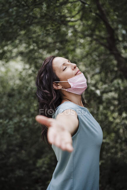 Mid adult woman standing with arm outstretched in forest during coronavirus outbreak — Stock Photo