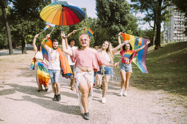 Feliz amigos masculinos e femininos com bandeiras de arco-íris andando no parque — Fotografia de Stock