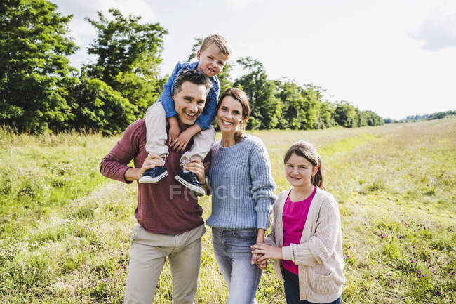 Чоловік, що носить хлопчика на плечах, стоячи з жінкою та дочкою на лузі. — стокове фото