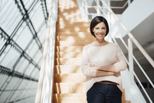 Mulher sorridente profissional com braços cruzados contra degraus no corredor — Fotografia de Stock