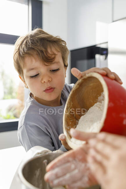 Хлопчик поливає борошно в електричному мікшері на кухні — стокове фото