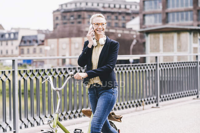 Улыбающаяся женщина пригородного колеса велосипед во время разговора по мобильному телефону в городе — стоковое фото