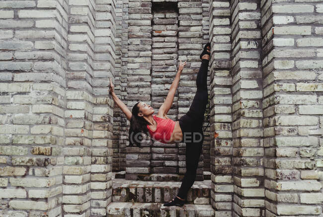 Молодая женщина растягивает ногу на каменной стене — стоковое фото