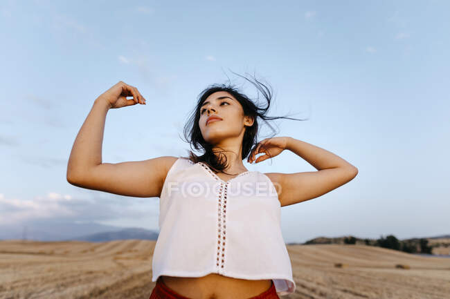 Молода жінка з піднятими руками танцює на полі під час заходу сонця. — стокове фото