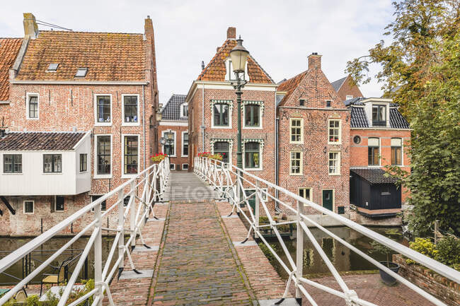 Niederlande, Provinz Groningen, Appingedam, Fußgängerbrücke über den Damsterdiep-Kanal mit gemauerten Stadthäusern im Hintergrund — Stockfoto