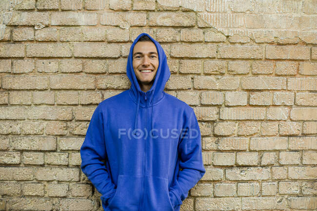 Smiling male athlete in blue jacket against brick wall — Stock Photo