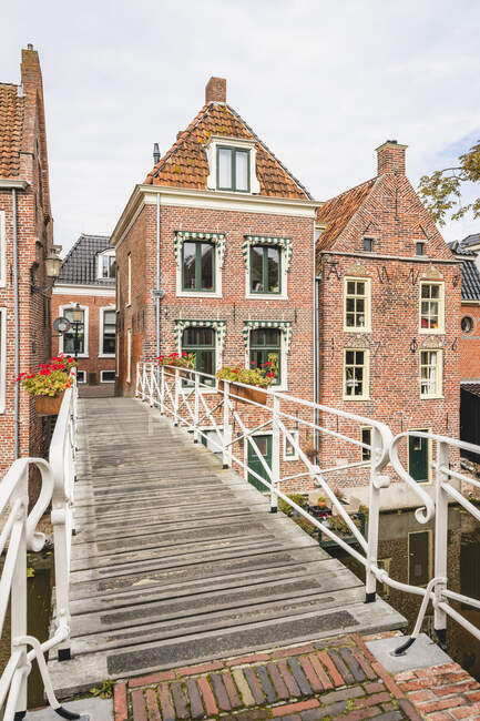 Niederlande, Provinz Groningen, Appingedam, Fußgängerbrücke über den Damsterdiep-Kanal mit gemauerten Stadthäusern im Hintergrund — Stockfoto