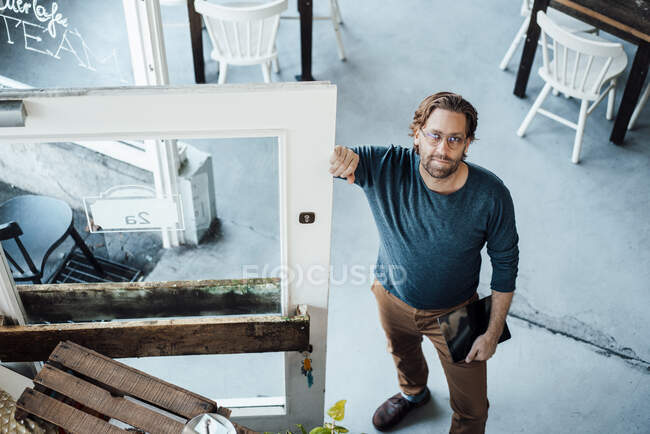 Propriétaire masculin avec tablette numérique debout à côté de la porte au café — Photo de stock