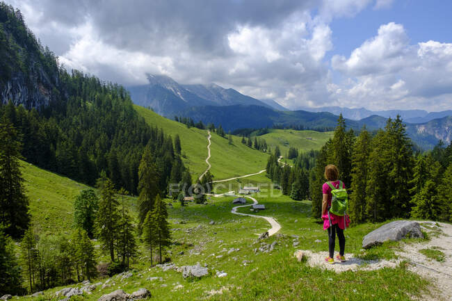 Женщина-туристка стоит посреди пешеходной дорожки, извиваясь по летней долине в Берхтесгаденских Альпах — стоковое фото