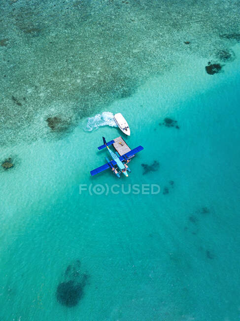 Вид с воздуха на моторную лодку, приближающуюся к гидросамолёту, плавающему в бирюзовой воде мужского атолла — стоковое фото