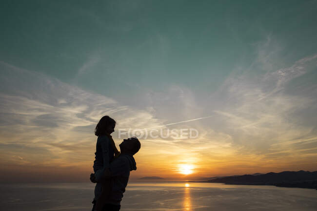 Father in silhouette carrying daughter during sunset — Stock Photo