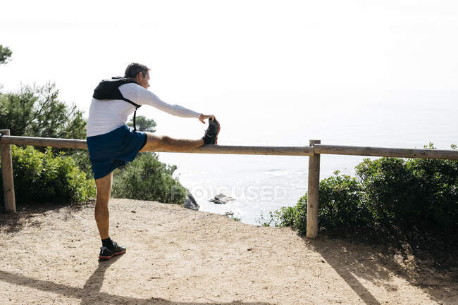 Man stretching on wooden railing during sunny day — Stock Photo