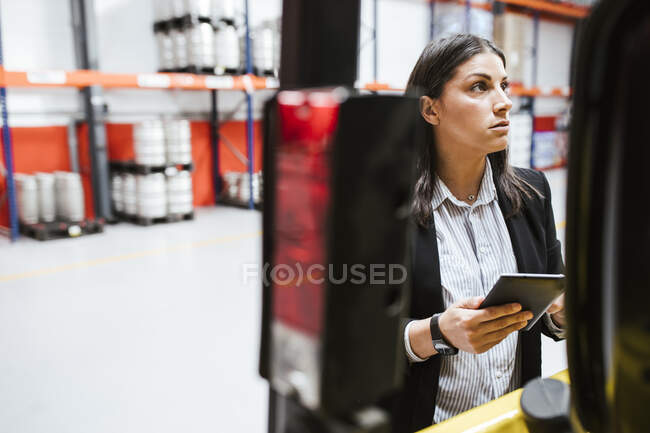 Profissional feminino olhando para longe enquanto segurava tablet digital em armazém iluminado — Fotografia de Stock