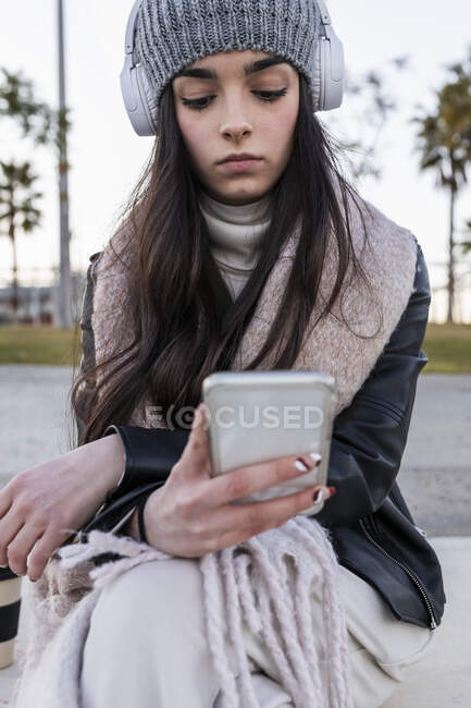 Ragazza adolescente utilizzando il telefono cellulare mentre seduto sulla panchina al parco — Foto stock