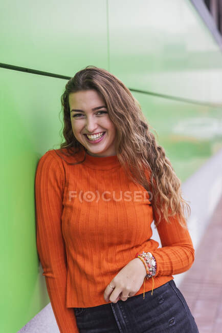 Mujer feliz apoyada en la pared verde - foto de stock