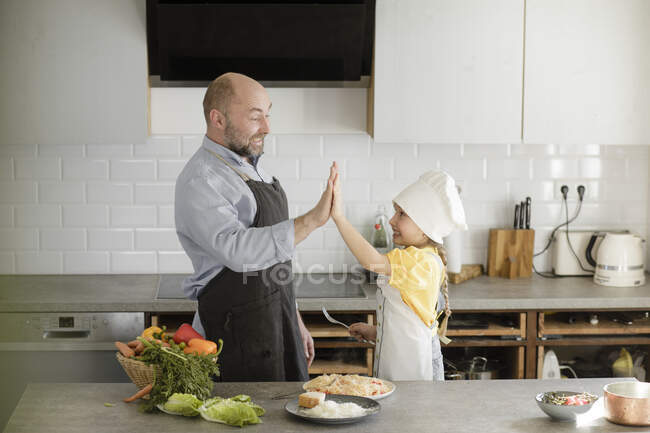 Mature men and girl cheering with giving high-five while standing in kitchen at home — Stock Photo