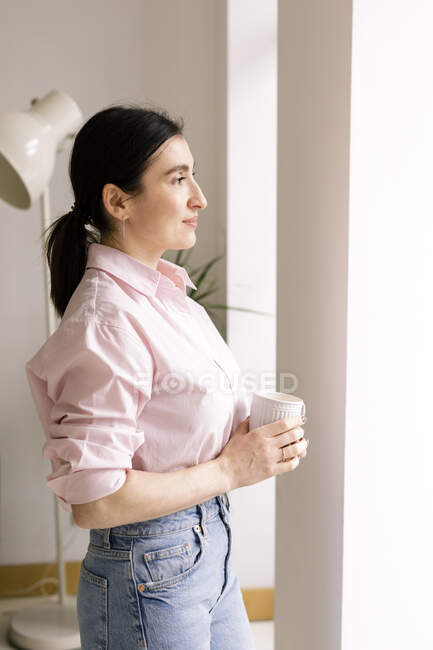 Thoughtful businesswoman in smart casual holding coffee mug at home — Stock Photo