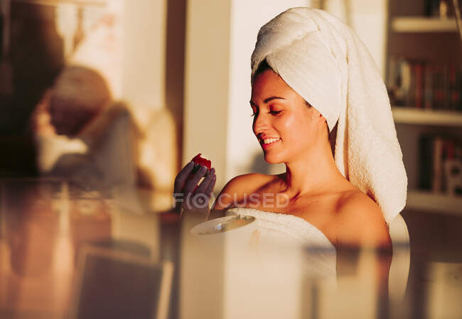 Smiling woman wearing towel eating strawberry at home — Stock Photo