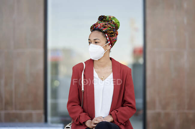 Женщина в платке и защитной маске смотрит в сторону, сидя на улице — стоковое фото