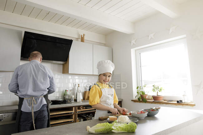 Smiling girl cutting vegetable while standing in kitchen at home — Stock Photo