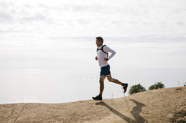 Чоловік біжить на брудній дорозі проти хмарного неба в сонячний день — стокове фото