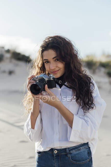 Belle jeune femme avec caméra vintage debout contre le ciel — Photo de stock
