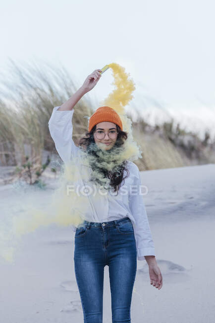 Jovem mulher no cabelo de malha laranja com flare de angústia em pé contra o céu na praia — Fotografia de Stock