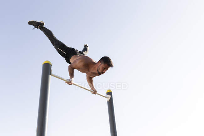 Active male athlete exercising on horizontal bar in park against clear sky — Stock Photo