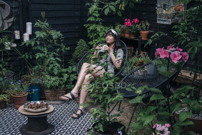 Mulher segurando xícara de café enquanto sentado pernas cruzadas no joelho na cadeira — Fotografia de Stock