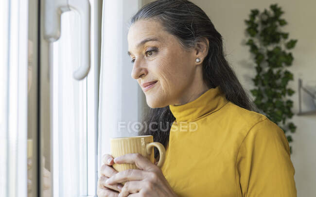 Donna matura contemplando mentre tiene la tazza di caffè a casa — Foto stock