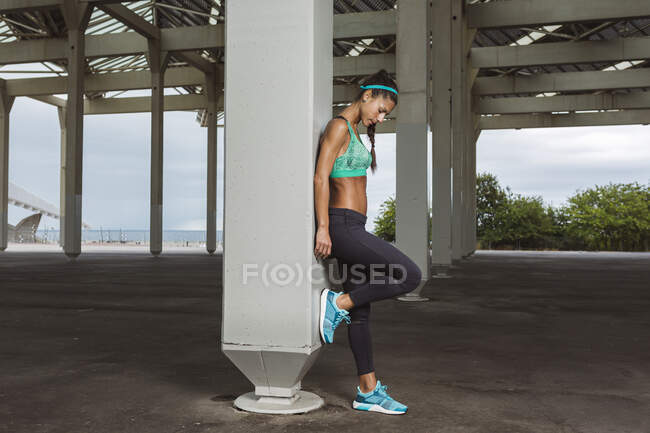 Female athlete looking down while leaning on pillar — Stock Photo