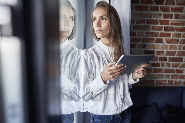 Бизнесвумен с цифровым планшетом смотрит в окно дома — стоковое фото