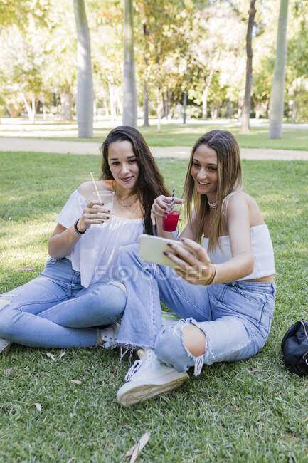 Amigos do sexo feminino segurando bebidas enquanto toma selfie no parque — Fotografia de Stock