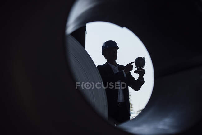Businessman holding globe while standing in steel mill — Stock Photo