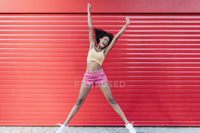 Joyeux jeune femme avec les yeux fermés sautant devant obturateur rouge — Photo de stock