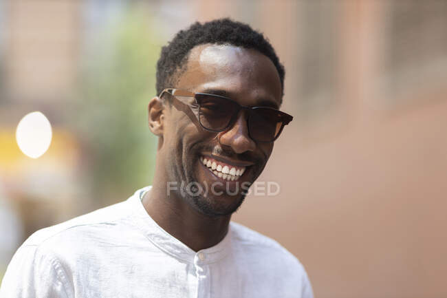 Jeune homme en lunettes de soleil souriant pendant la journée — Photo de stock