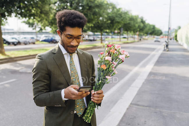 Geschäftsmann mit Blumenstrauß mit Handy auf der Straße — Stockfoto