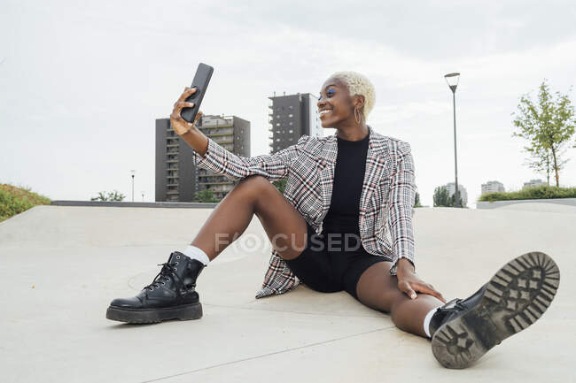 Улыбающаяся женщина делает селфи через смартфон, сидя на тропинке — стоковое фото