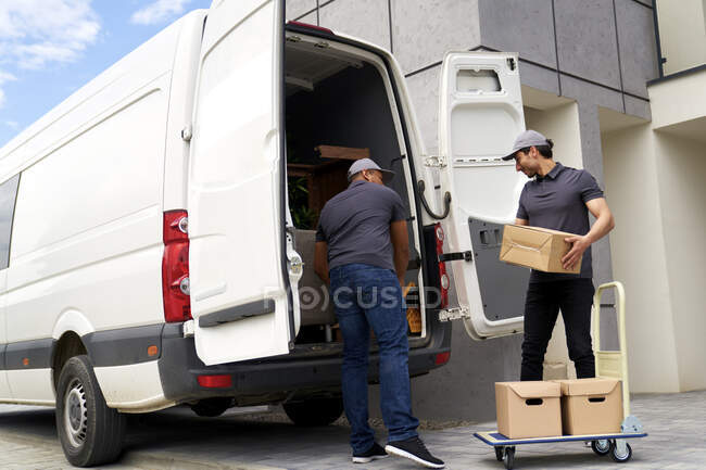 Entrega hombres carga caja de cartón en furgoneta - foto de stock