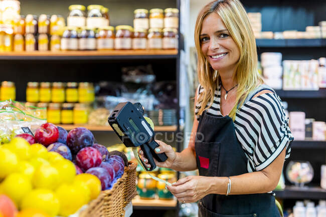 Vendedora madura etiquetando frutas en tienda ecológica - foto de stock