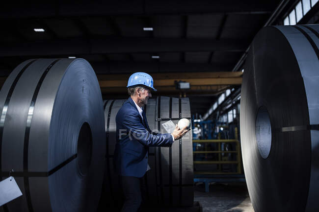 Uomo d'affari con hardhat tenere globo mentre in piedi presso l'industria siderurgica — Foto stock